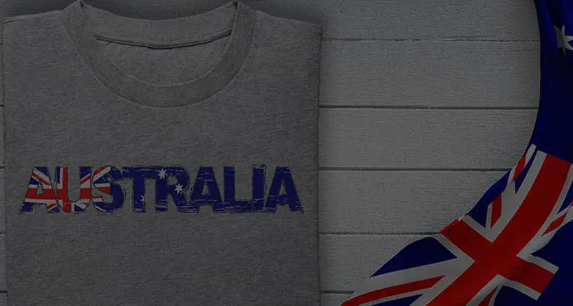 Grey folded T-shirt with “AUSTRALIA” artwork in flag colours beside fabric with Australian flag detail—Australian owned custom apparel from T Shirts Australia.