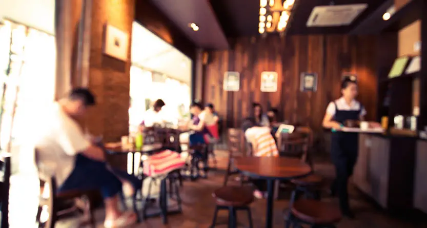 Soft-focus interior of a busy coffee shop with warm lighting—staff and customers in a café setting where branded tees and aprons build recognition.