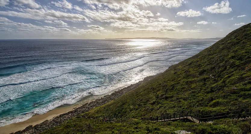 Coastal Western Australia scenery—turquoise ocean, surf, and green headland with a boardwalk—representing WA customers ordering custom tees with Australia-wide delivery.