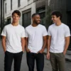 Custom printed bulk AS Colour Staple white T-shirts lifestyle group White AS Colour Staple T-shirts worn by three men outdoors Premium retail-quality tees shown in a real-world setting Clean white garments suitable for custom printing Group styling ideal for bulk orders and merchandise