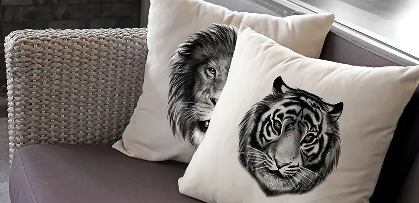 Close-up of two custom-printed cushion covers on a cane outdoor sofa—one with a black-and-white tiger print, one with a lion—showing detail of fabric and print quality.