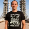 Man wearing a black I Really Need More Space Men T Shirt standing in front of a rocket launch pad
