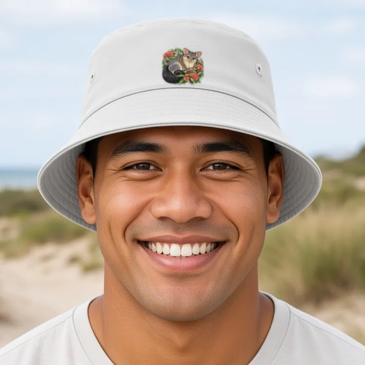 Smiling man with short dark hair on a sandy beach track through coastal dunes, face to camera, wearing the white Brushtail Possum Among Eucalyptus Blooms bucket hat